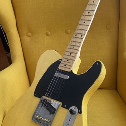 Žlutá elektrická kytara s tvarem typu Telecaster a černým pickguardem. Na hlavě hředu je viditelné logo Fender. Tělo kytary vykazuje výrazné opotřebe…