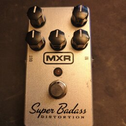 Stříbrný efekt pedál s pěti černými ovládacími knoflíky. Na přední straně je umístěno logo MXR, nápis Super Badass a pod ním slovo DISTORTION. V horn…