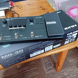 Černý kytarový procesor NUX MG-30 položený na své originální krabici s nápisem MG-30 VERSATILE MODELER. Zařízení má digitální displej, několik ovláda…