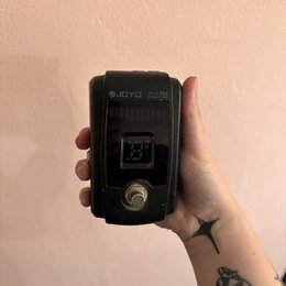 Černý ladicí pedál s digitálním displejem. Na horní části je bílým nápisem značka JOYO a model JT-305 CHROMATIC TUNER. Povrch zařízení vykazuje drobn…