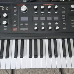 Černý synthesizér s bílými a černými klávesami. V levém horním rohu je logo ASM ASHLEY VOLUME MACHINES a nápis HYDRASYNTH. Panel obsahuje množství ov…