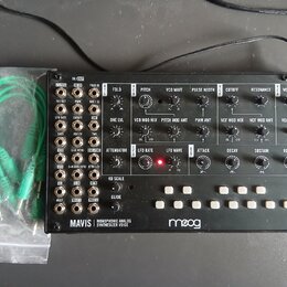 Černý analogový syntetizátor s bílými nápisy a ovládacími prvky. Na spodní liště je uveden název MAVIS MONOPHONIC ANALOG SYNTHESIZER VOICE a logo moo…