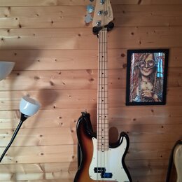 Elektrická basová kytara s trupem v barevném přechodu od černé přes hnědou k žluté (sunburst) a bílým pickguardem. Na hlavě hmatníku je viditelné log…