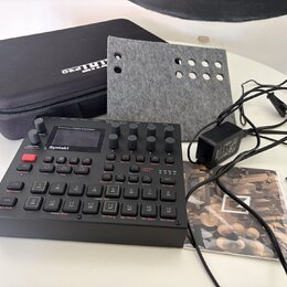 Černý digitální sekvencer a syntetizátor s nápisem Syntakt a pod ním menším písmem Elektron. Zařízení obsahuje řadu tlačítek, otočných knoflíků a mal…