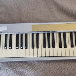 Stříbrný MIDI kontrolér s klávesnicí. Na horním panelu je zlatý pruh s nápisem M-AUDIO KEYSTATION 61mkII. Bílé klávesy vykazují zežlutnutí, na stříbr…