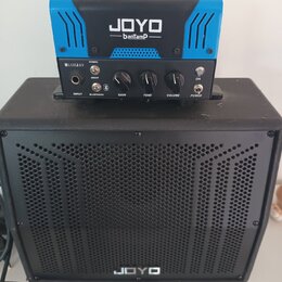Modrý kytarový zesilovač s černou rukojetí a nápisem JOYO banTamp položený na černé kytarové reproducing s nápisem JOYO. Na předním panelu zesilovače…