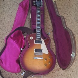 Elektrická kytara s tónem sunburst v hnědých a žlutých odstínech, bílým pickguardem a dvěma humbuckery. Nástroj je umístěn v otevřeném hnědém tvrdém…