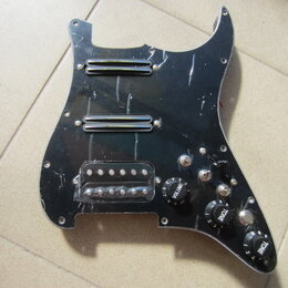 Černý plastový pickguard pro elektrickou kytaru s třмя snímači. Horní dva jsou humbuckery s chromovaným krytem, spodní je singl v průhledném plastové…