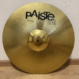 Zlatý mosazný činel s koncentrickými drážkami na povrchu. Na horní části je černý nápis pAiste, pod ním text 16" CRASH a vedle něj označení 101 BRASS…