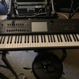 Černý digitální klavír umístěný na černém stojanu. V pravém horním rohu je bílý nápis KRONOS Xsynth. Nástroj má v horní části ovládací prvky, tlačítk…