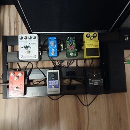 Kytarový efektový pedalboard s dvěma řadami pedálů. V horní řadě jsou od levy pedály s nápisy JOYO Classic Flanger, Boss BF-2 Flanger, nečitelný zele…