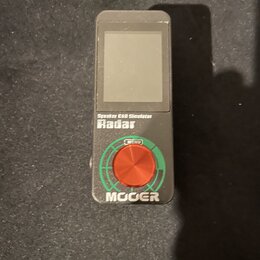 Černý obdélníkový přístroj s displejem. Na přední straně jsou nápisy Speaker CAB Simulator a Radar, pod nimi se nachází červené ovládací kolečko s ná…