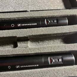 Dvě černá kondenzátorová mikrofony umístěná v šedém pěnovém pouzdře. Na obou je bílý nápis SENNHEISER s doprovodným logem a červený přepínač s nápise…