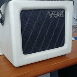 Bílý kytarový kombozesilovač s černou textilní maskou reproduktoru s diagonálními pruhy. Na předním panelu je umístěno stříbrné logo VOX a na černém…