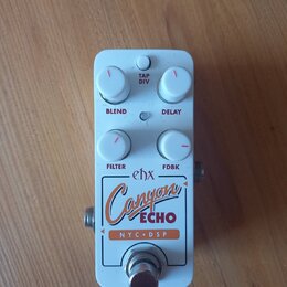 Bílý efektový pedál s nápisy ehx, Canyon ECHO a NYC DSP. Na horní straně jsou čtyři bílé otočné knoflíky s červenými značkami a popisky BLEND, DELAY,…