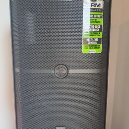 Černý reproduktor s kovovou mřížkou. Na horní části je nalepený štítek s nápisy SRM V-CLASS, SERIOUS OUTPUT 1000W OF SOLID POWER, CUTTING-EDGE TECHNO…