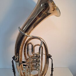 Zlatavý mosazný tuba v černé stojce. Na vnitřní straně zvonu je vidět zlatý nápis "Yamaha". Nástroj vykazuje známky běžného používání v podobě drobný…