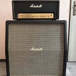 Kytarový zesilovač a reprobox značky Marshall. Zesilovací hlava má černý povrch s bílým nápisem Marshall a zlatý ovládací panel s nápisy ORION 50, Ga…