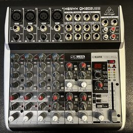 Šedý mixážní pult značky behringer s nápisem XENYX QX1202USB. Zařízení obsahuje několik vstupních kanálů s ovládacími prvky pro GAIN, EQ a FX, USB IN…