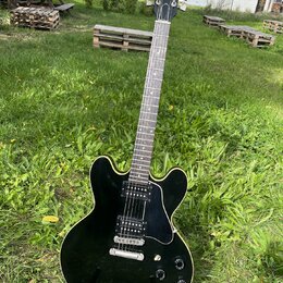 Černá elektrická kytara s polodupatým tělem a bílým lemováním. Na hlavě hředu je viditelné logo Gibson. Nástroj má dva humbuckery, čtyři ovládací kno…