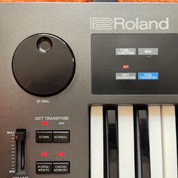 Detailní pohled na ovládací panel klávesového nástroje značky Roland. Na šedém povrchu je umístěn velký černý otočný ovladač s nápisem α-DIAL a někol…