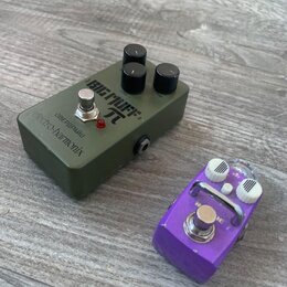 Na fotografii jsou dva efektové pedály na dřevěné podlaze. Větší pedál je olivově zelený s nápisy BIG MUFF π, electro-harmonix a ОВЕРДРАЙВ. Menší ped…