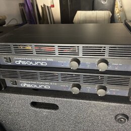 Dvě černé rackové konce s nápisem Professional Power Amplifier QSA-600 a logem QSOUND. Každý přístroj má v přední části vypínač, dva ovratové ovládac…