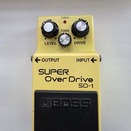 Žlutý efekt pedál s černým gumovým spínacím pedalem. Na zařízení jsou nápisy SUPER Over Drive, SD-1 a logo BOSS. Horní panel obsahuje tři ovládací kn…