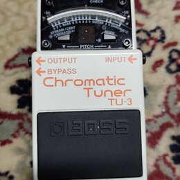 Bílý kytarový ladič značky BOSS, model Chromatic Tuner TU-3. Na horní straně je analogový displej s nápisy CHECK, PITCH a označením tónů. V horní čás…