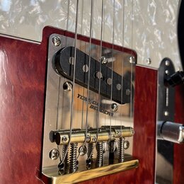 Detail elektrické kytary s červeným lakovaným tělem a bílým perleťovým pickguardem. Je zde vidět černý humbucker s nápisem TOM AND BENDERS a zlatý ko…