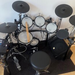 Elektronická bicí souprava značky Roland v černé barvě s bílými bubny. Na bubnech je viditelné logo Roland a nápis V-Drums. Součástí sady je ovládací…
