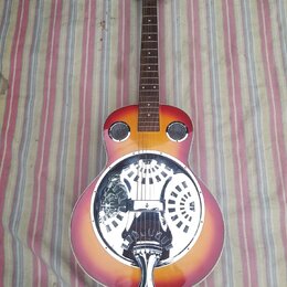Resonátorová kytara s červeno-žlutým přechodem barvy (sunburst). Tělo obsahuje velký chromovaný resonátor s ornamentálním výřezem a dva malé kruhové…