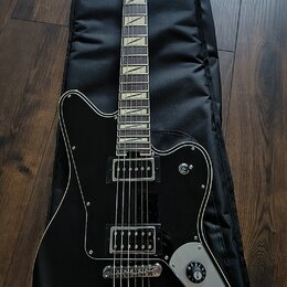 Černá elektrická kytara s hnědým hрифem a bílými vložkami na hmatníku, položená na černém obalu. Na hlavě je viditelné logo "Gretsch". Kytara má dva…