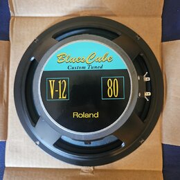 Kruhové reproduktory v černé kovové rámu, umístěné v kartónovém boxu. Na středovém krytu jsou nápisy „Blues Cube Custom Tuned“, „V-12“ a „80“ v žlutý…