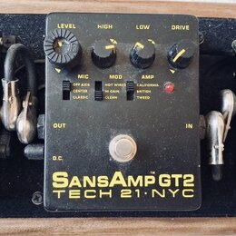 Černý efekt pedál s nápisy SansAmp GT2 a TECH 21 NYC. Na horní straně jsou čtyři ovládací knoflíky s popisky LEVEL, HIGH, LOW a DRIVE. Pod nimi se na…