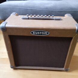 Kytarový kombo zesilovač v hnědém vinylovém potahu s kovovými rohy. Na přední straně je umístěno oválné logo s nápisem KUSTOM a pod ním hnědý textiln…