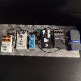 Sestava efektů na stříbrném kovovém pedalboardu s protiskluzovou strukturou. Zleva jsou vidět pedály s nápisy: „PHASER CORE“ a „nux“, „NUX ANALOG DEL…