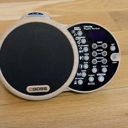 Elektronický doprovodný nástroj v dřevěném provedení s černým mluvčím členem. Na přístroji je uveden nápis BOSS a model DR-01s Rhythm Partner. Ovláda…