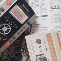 Stříbrný perkusní zvukový modul značky Roland s názvem modelu PERCUSSION SOUND MODULE TD-9. Zařízení má černý ovládací panel s několika tlačítky, kro…