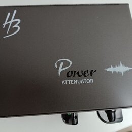 Černý kovový box s nápisem Power ATTENUATOR a grafickým symbolem zvukové vlny. V levém horním rohu je bílé logo znázornující stylizované písmeno H s…