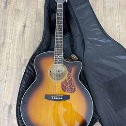 Akustická kytara s vyvedeným korpusem v provedení sunburst, položená v černém měkkém pouzdře. Na hlavě nástroje je bílý nápis GUILD. Kytara má hnědý…