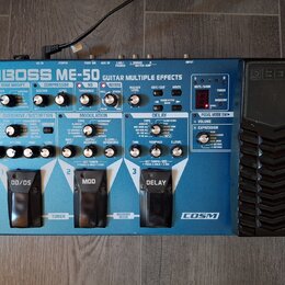 Modrý efektový pedál Boss ME-50 Guitar Multiple Effects. Na horní straně jsou různé ovládací knofíky, přepínače a červené digitální displeje. V dolní…