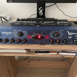 Modrý kytarový procesor s kovovým šasi a názvem V-AMP PRO a logem BEHRINGER. Na předním panelu jsou ovládací knofíky, červené tlačítka A až E a digit…