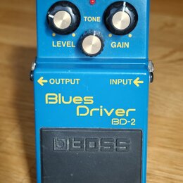 Modrý kytarový efekt s nápisy Blues Driver a BD-2. Na horní části jsou tři ovládací knoflíky s popisky LEVEL, TONE a GAIN a červená kontrolka CHECK.…