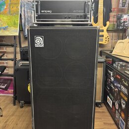 Sada basového zesilovače a reproduktorové skříně v černé barvě. Horní část obsahuje rack s nápisy SVPCL a ampeg SVT-300. Spodní reproduktorová skříně…