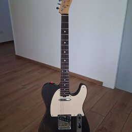 Elektrická kytara typu Telecaster s černým tělem a bílým pickguardem. Na hlavě hředu je viditelné logo "Laney". Nástroj má tmavý hmatník a je umístěn…