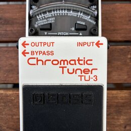 Bílý kytarový ladič značky BOSS, model TU-3 Chromatic Tuner. Horní část tvoří analogový displej s nápisy CHECK, -50, +50 a označením strun BASS a GUI…