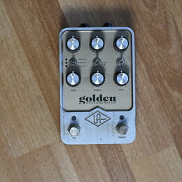 Stříbrný efekt pedál s nápisem golden REVERBERATOR a logem UA. Na horní části jsou tři ovládací knoflíky s popisky DECAY, PRE-DELAY a MIX, uprostřed…