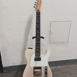 Světle béžová elektrická kytara s bílým pickguardem a hnědým hmatníkem. Na hlavě je viditelné logo Fender. Nástroj má dva snímače, jeden v pozici kob…