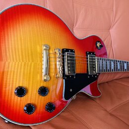 Elektrická kytara s trupem ve tvaru Les Paul v červeno-žlutém sunburst provedení s viditnou strukturou dřeva. Nástroj má dva humbuckery, čtyři černé…